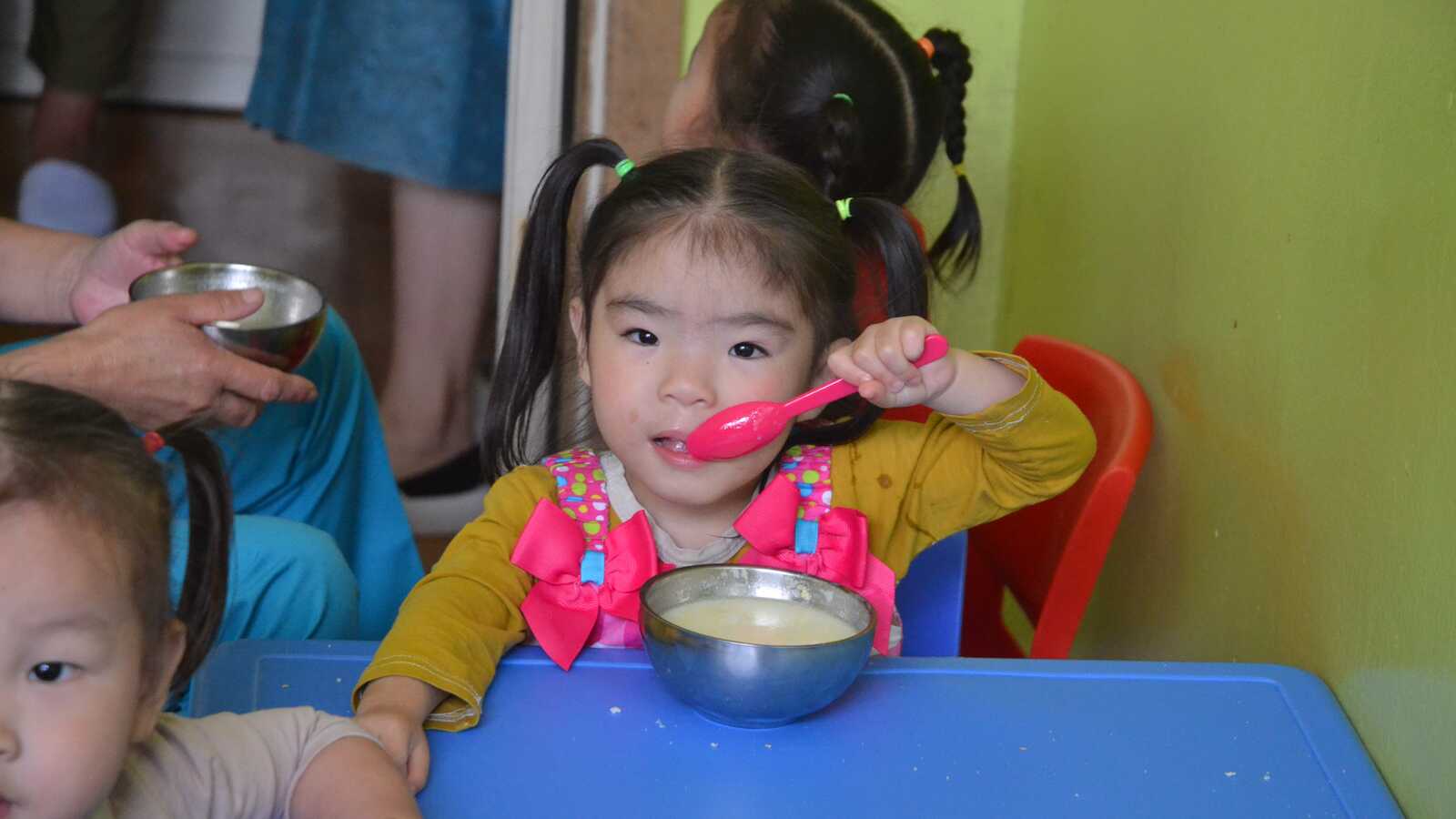 Little girl in Mongolia eating from a bowl with pink spoon