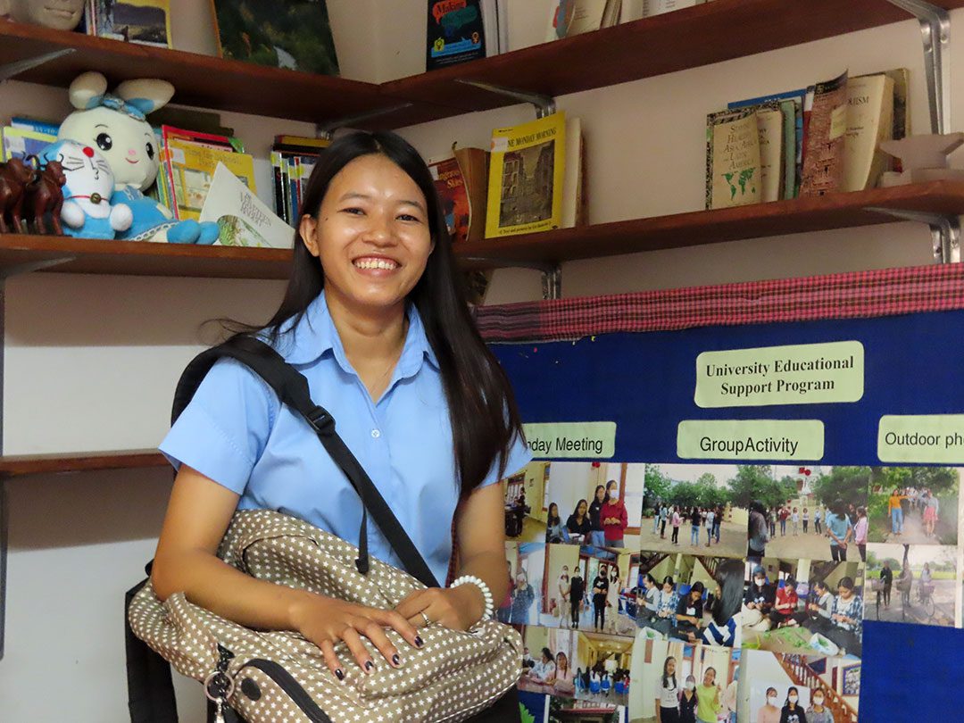 A university student in Cambodia smiles and shows her social work presentation