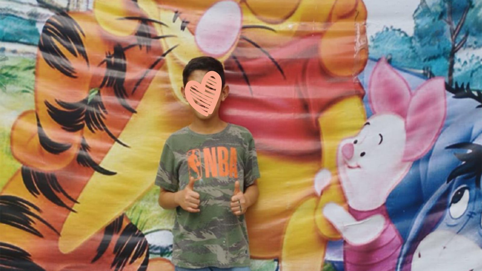 Young boy with heart over his face stands in front of a wall