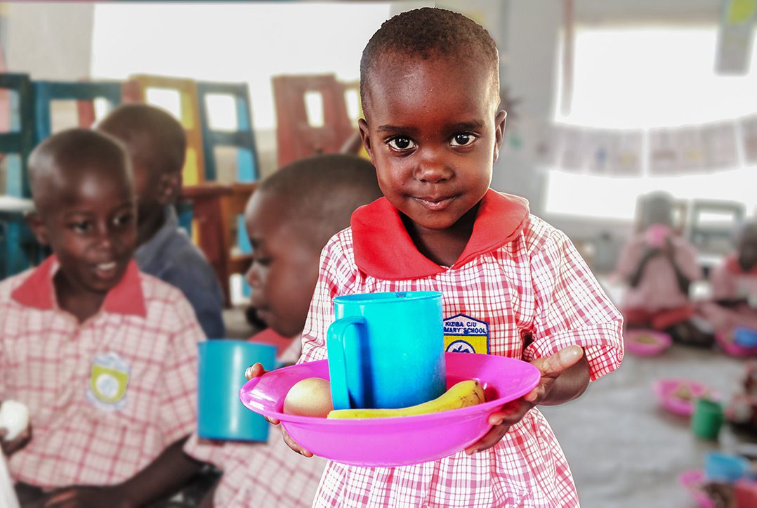 A preschooler in Uganda holds a tray of food