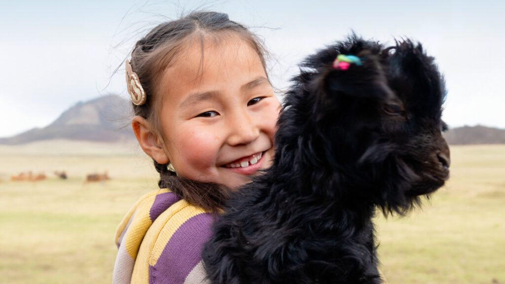 Little girl smiling while holding a black goat in a field