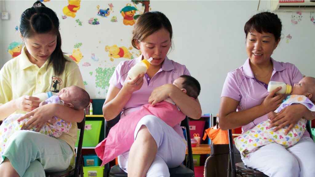 Three caregivers feeding three babies in an orphanage