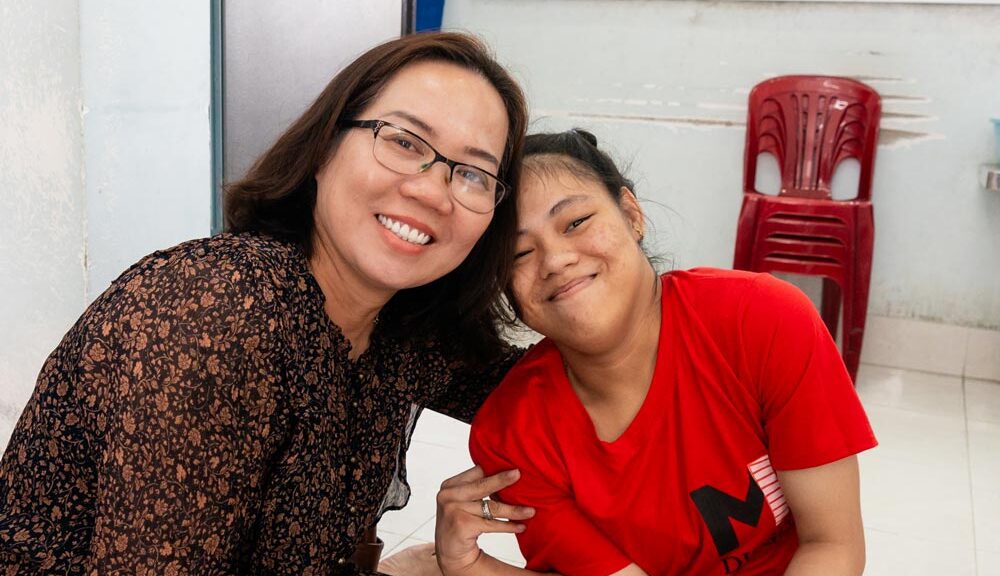 A girl growing up in an orphanage in Vietnam smiles with her caregiver.