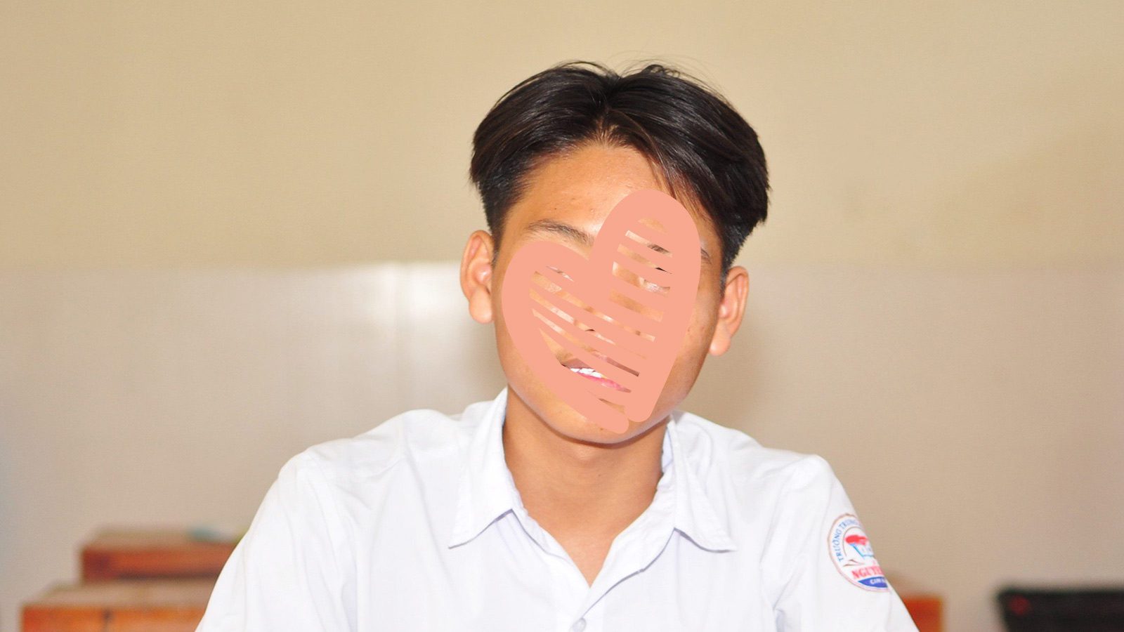 photo of a boy sitting at a desk in his school uniform with a waiting child heart over his face