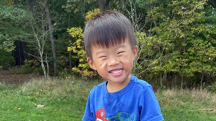 happy boy in a blue shirt smiling in a field in front of trees