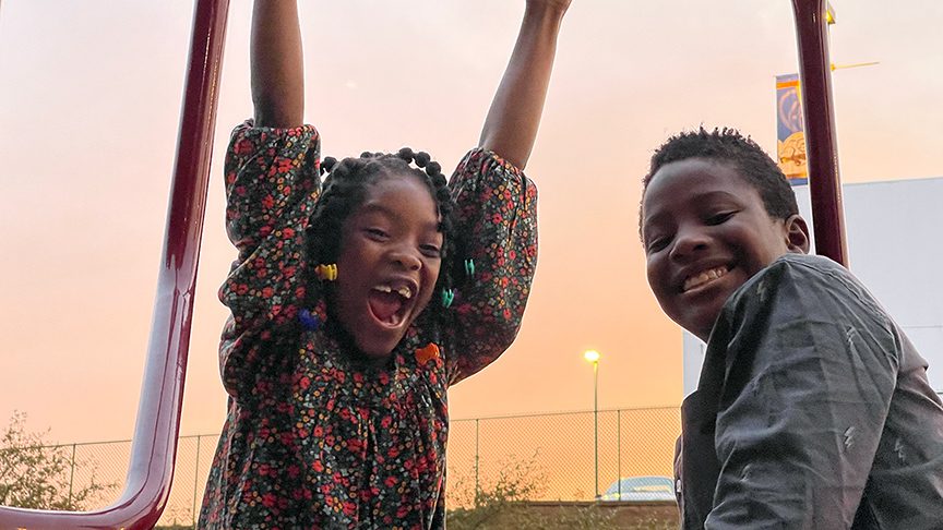 brother and sister smiling and playing on a playground in front of a sunset