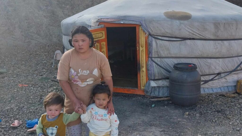 Mother and two small children stand outside a ger in Mongolia, cold weather support