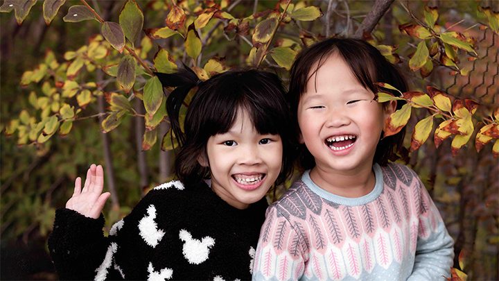 two sisters giggle in front of a bush in the fall season