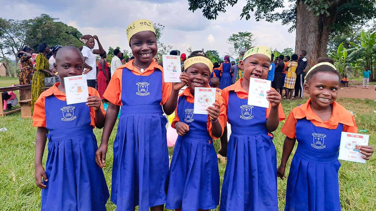 smiling girls in Uganda hold Christmas cards from their sponsors