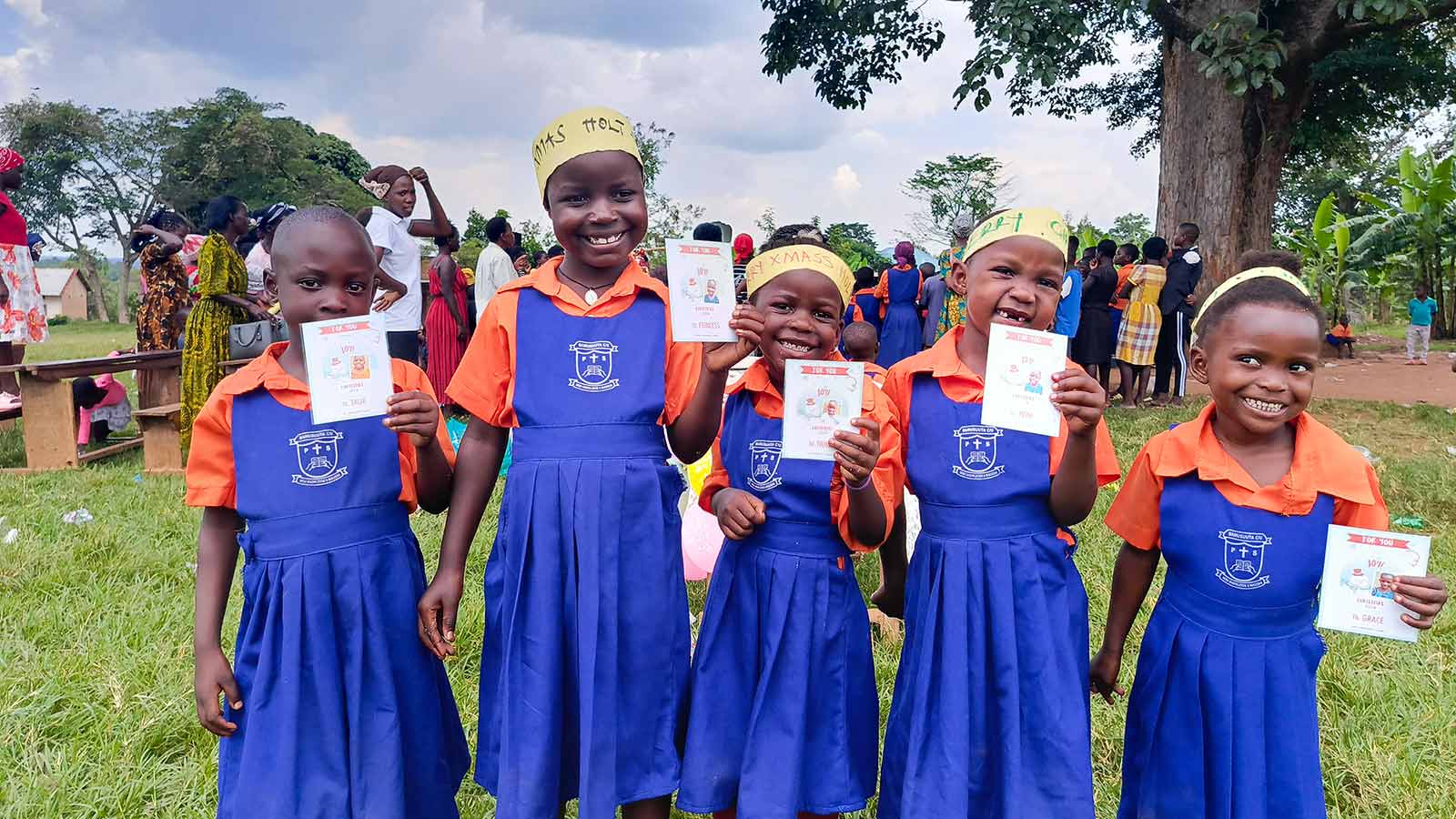 smiling girls in Uganda hold Christmas cards from their sponsors