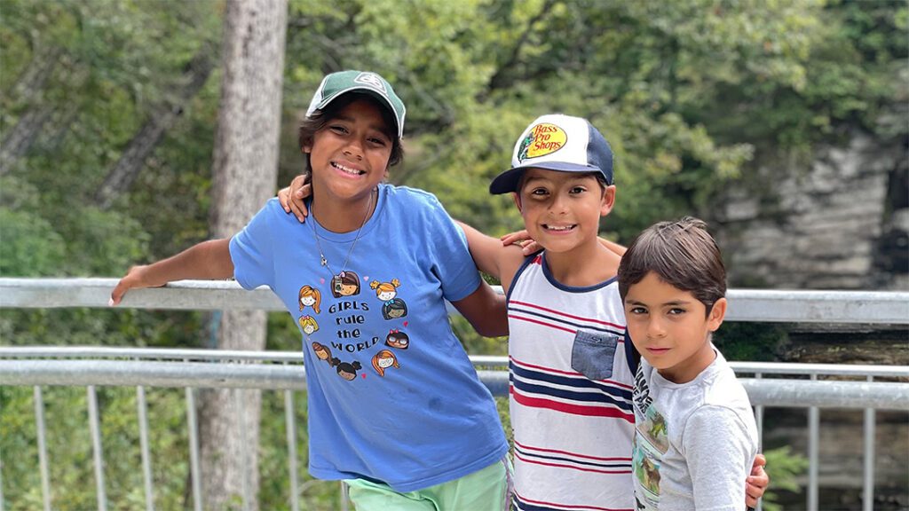 three siblings adopted from Colombia stand together with their arms around each other while standing on a bridge during a hike